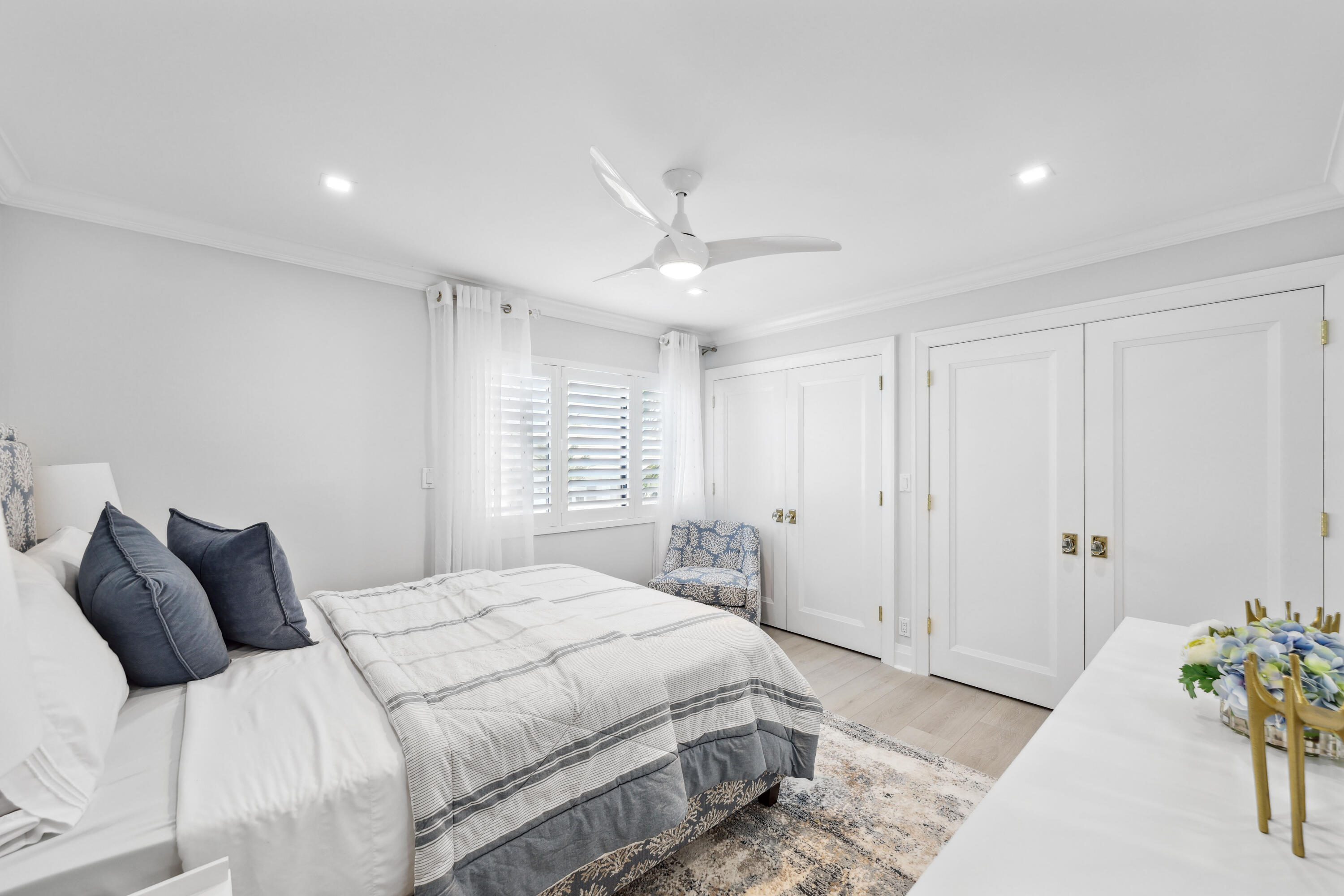 Furnished bedroom with a gray-striped bed, blue pillows, plantation shutters, and white paneled closet doors.