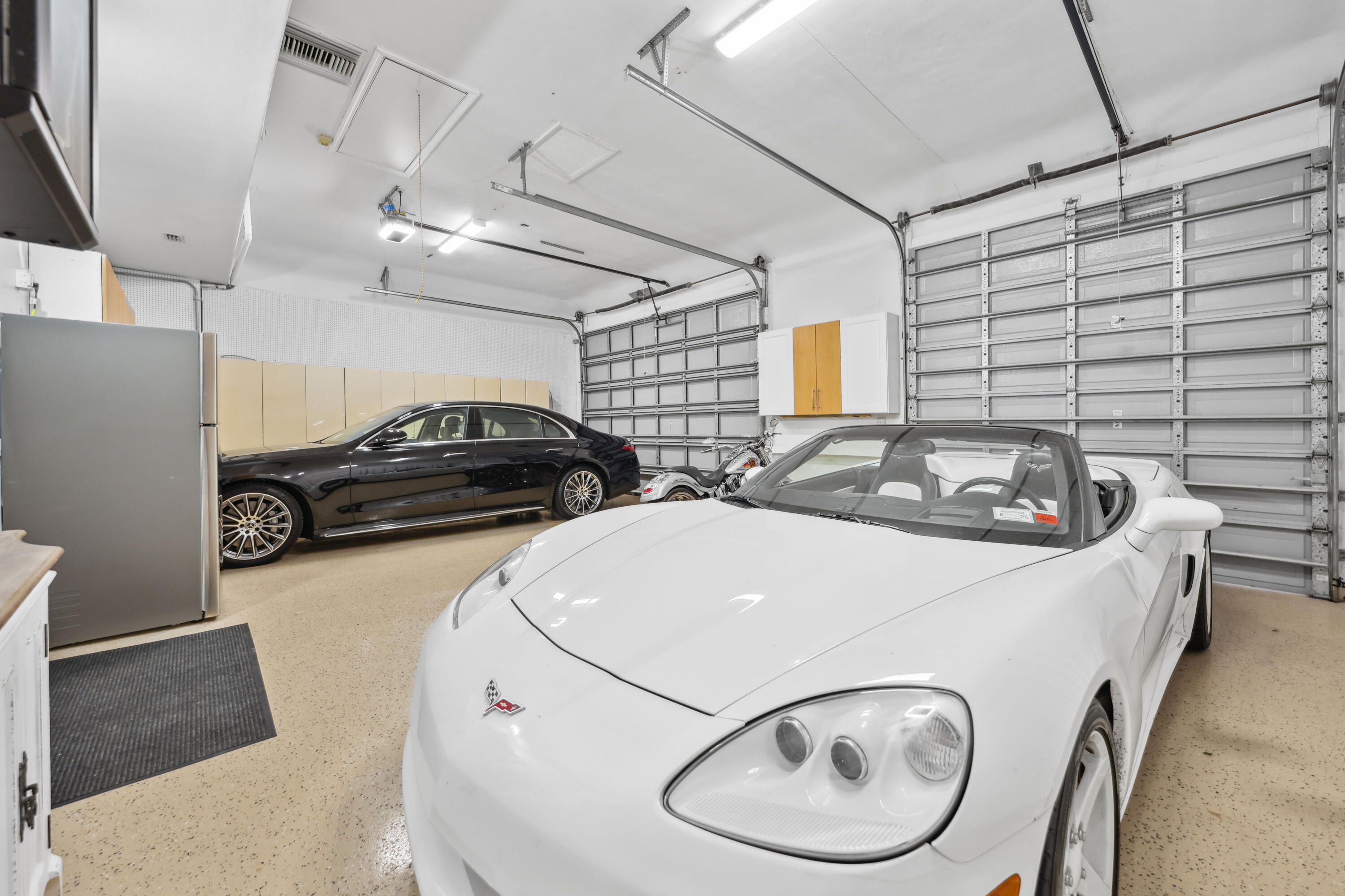Garage with a white convertible in the foreground and a black sedan behind it.