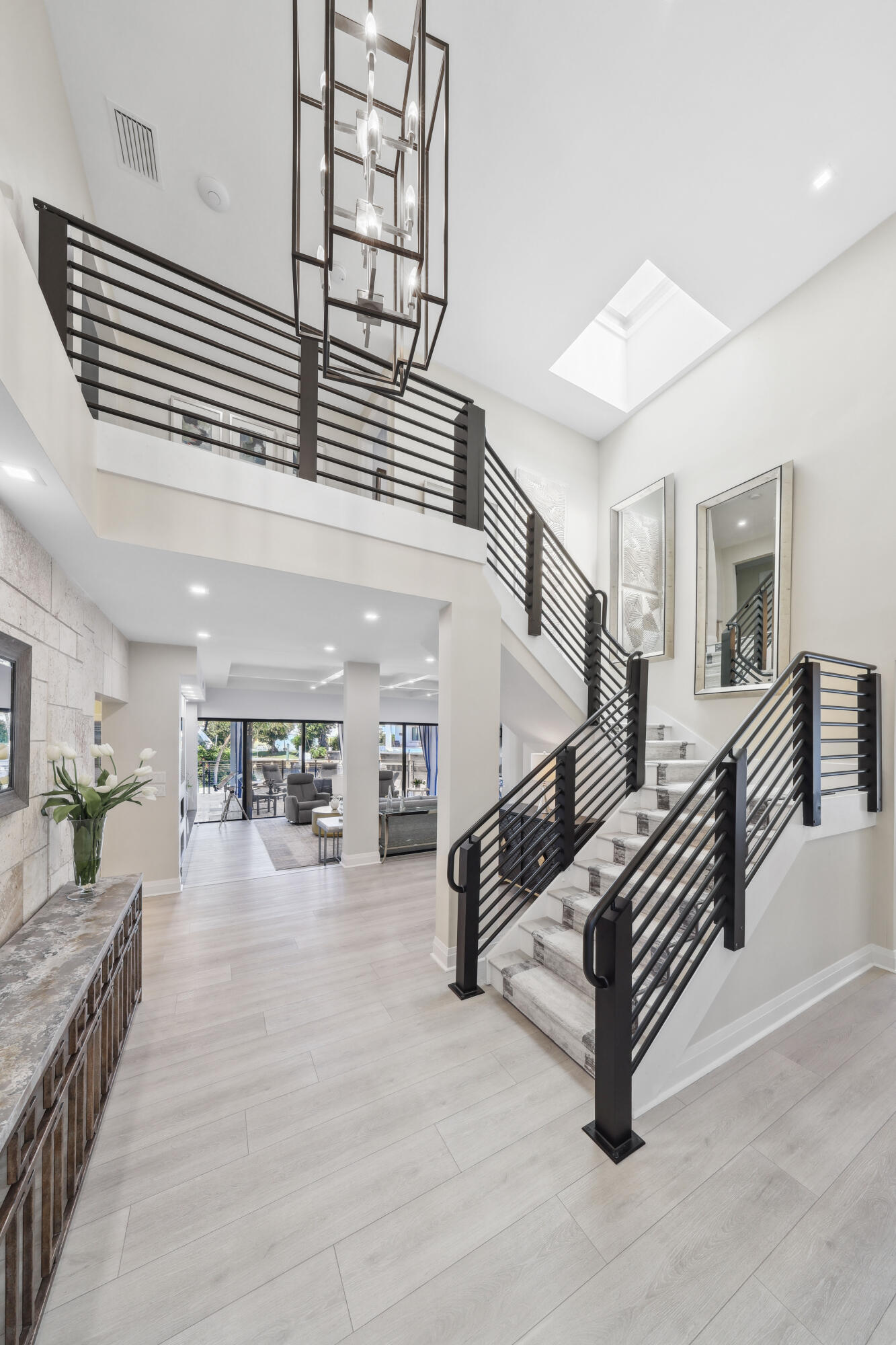 Double-height foyer with a black-railed staircase, geometric chandelier, and skylight.