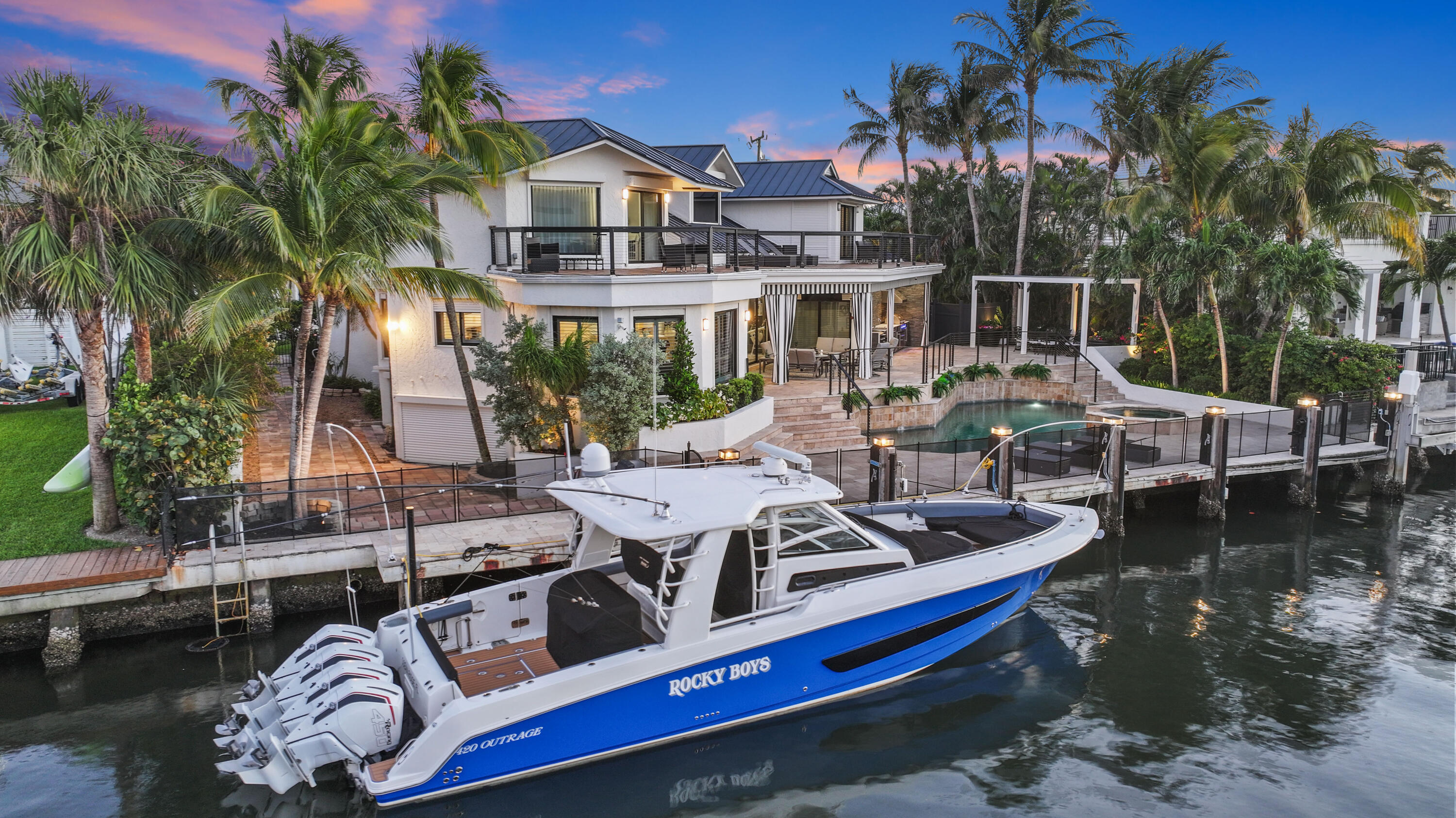 Waterfront home with a pool, dock, and blue-and-white boat at dusk.