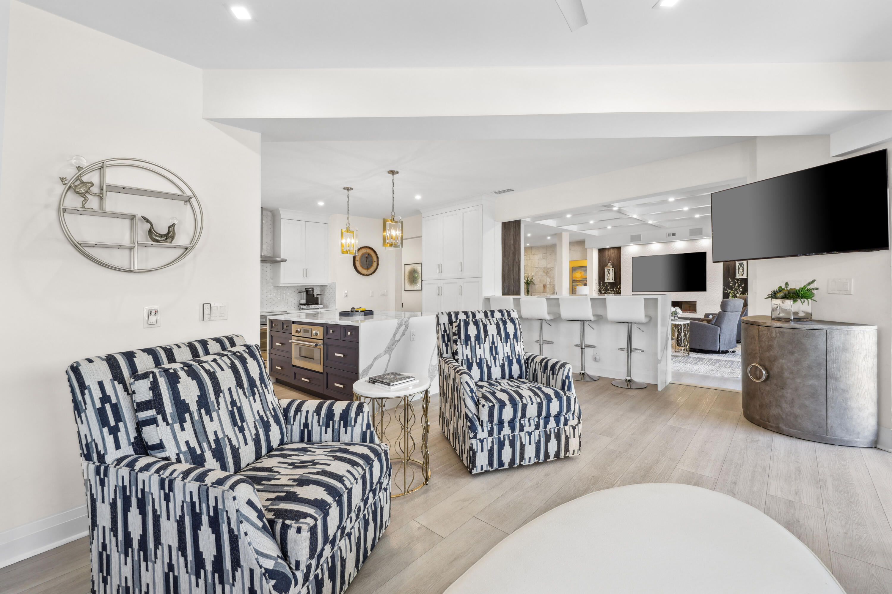 Open-plan living room and kitchen with patterned chairs, a marble island, and a second sitting area.