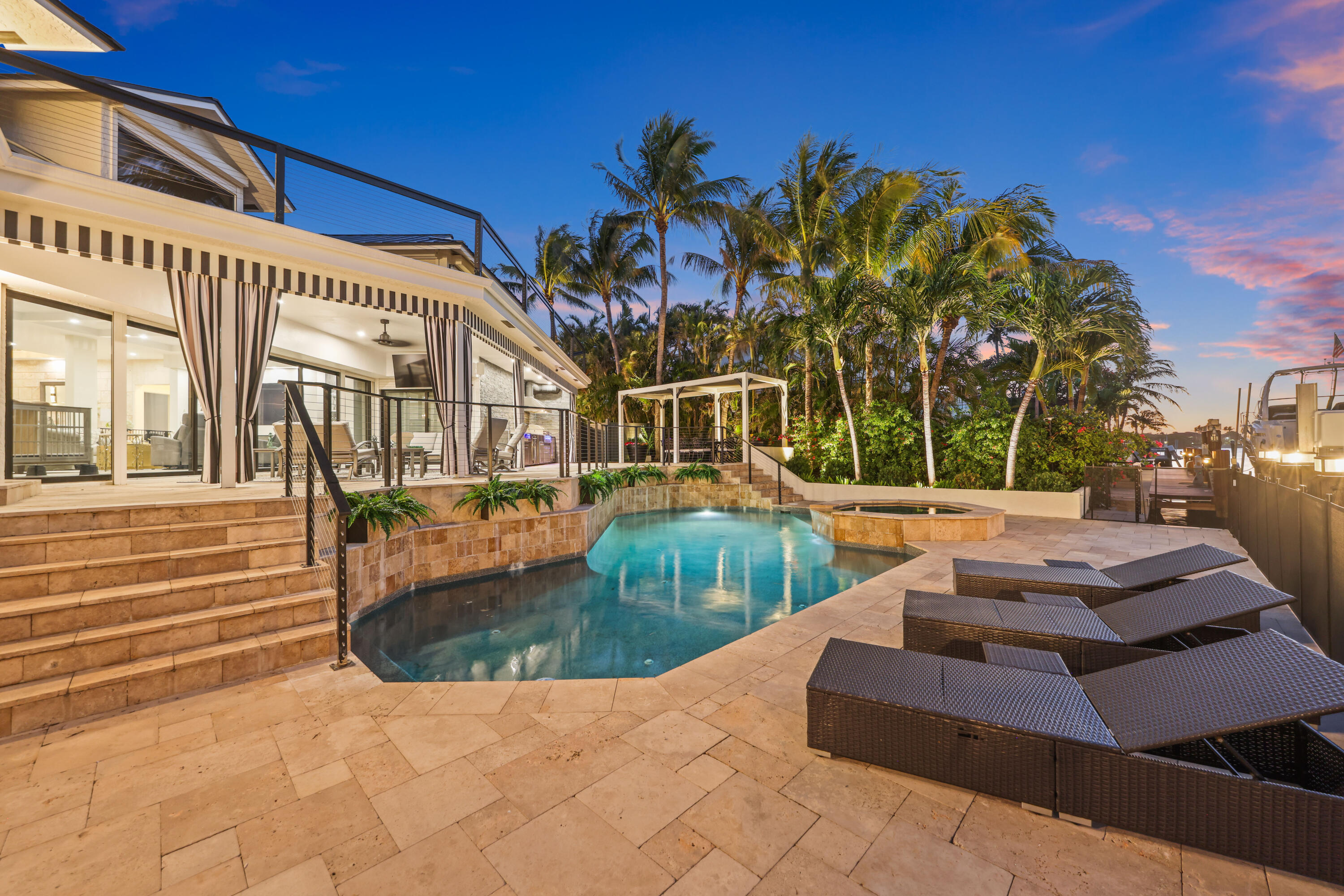 Backyard pool and stone patio with palm trees, lounge chairs, and a dock at dusk.