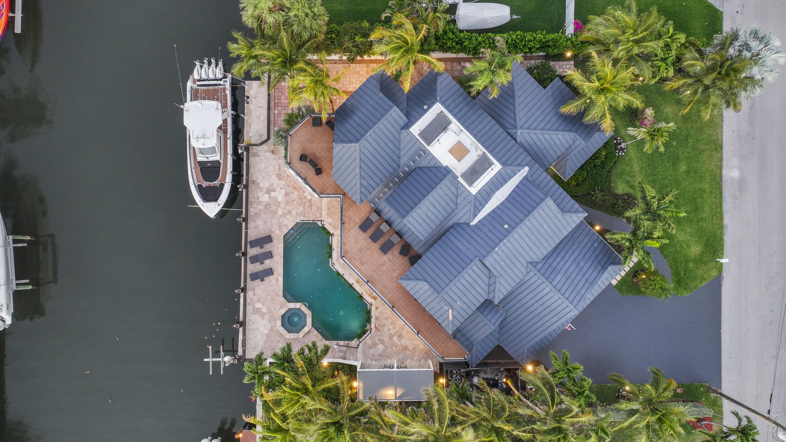 Waterfront home with a pool, spa, palm-lined lawn, and docked boat beside the canal.
