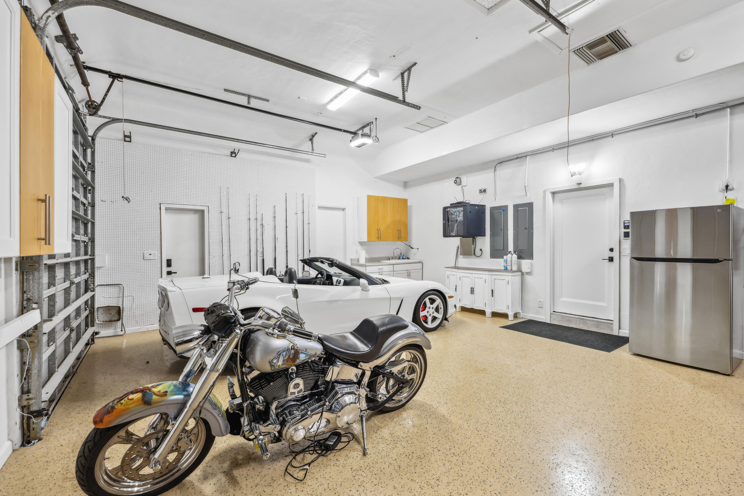 Garage with a white convertible and chrome motorcycle parked among built-in cabinets.