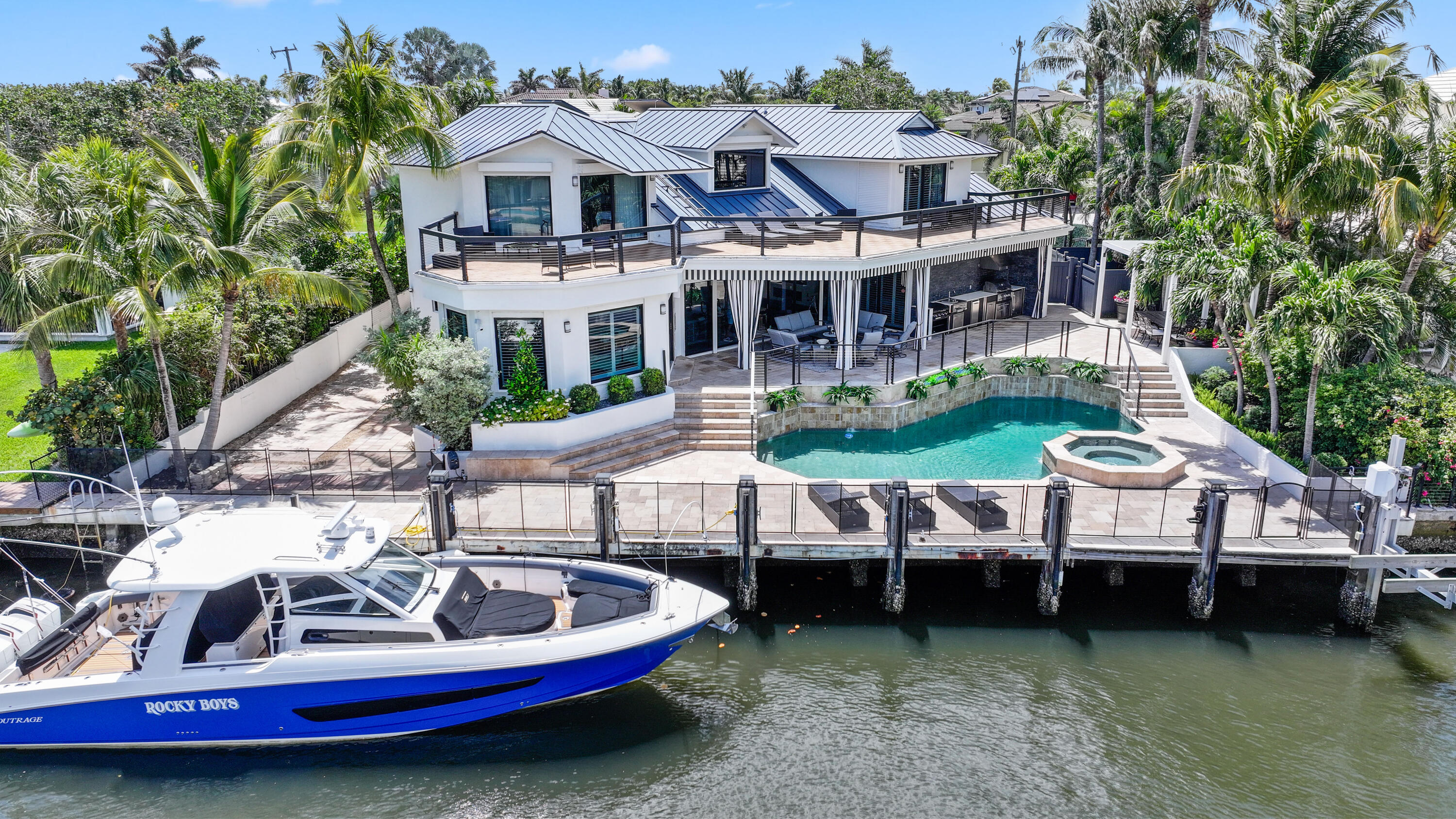 Waterfront home with wraparound terraces, pool and spa beside a docked blue-and-white boat.