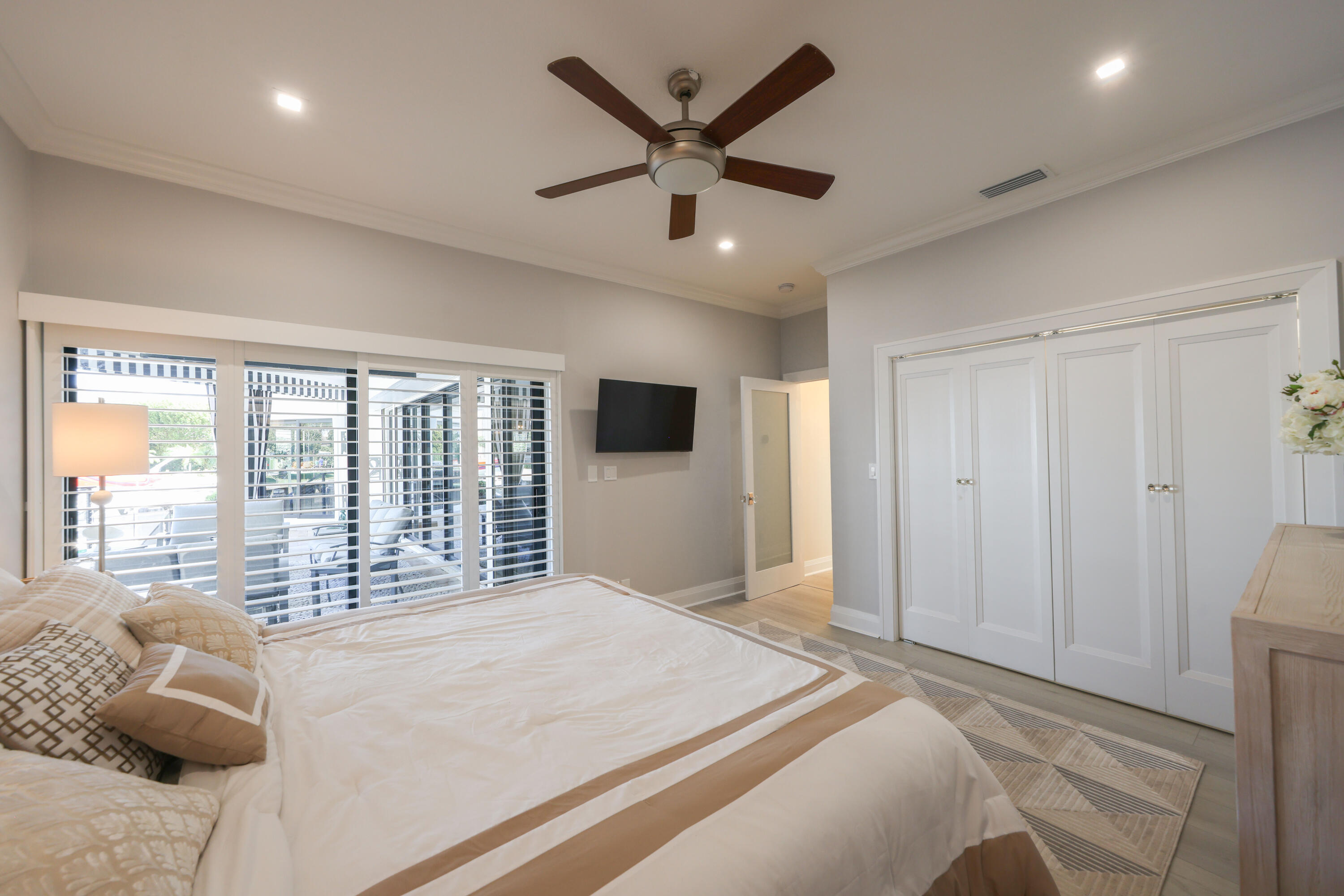 Bedroom with a white-and-beige bed, plantation shutters, and a dark wood ceiling fan.