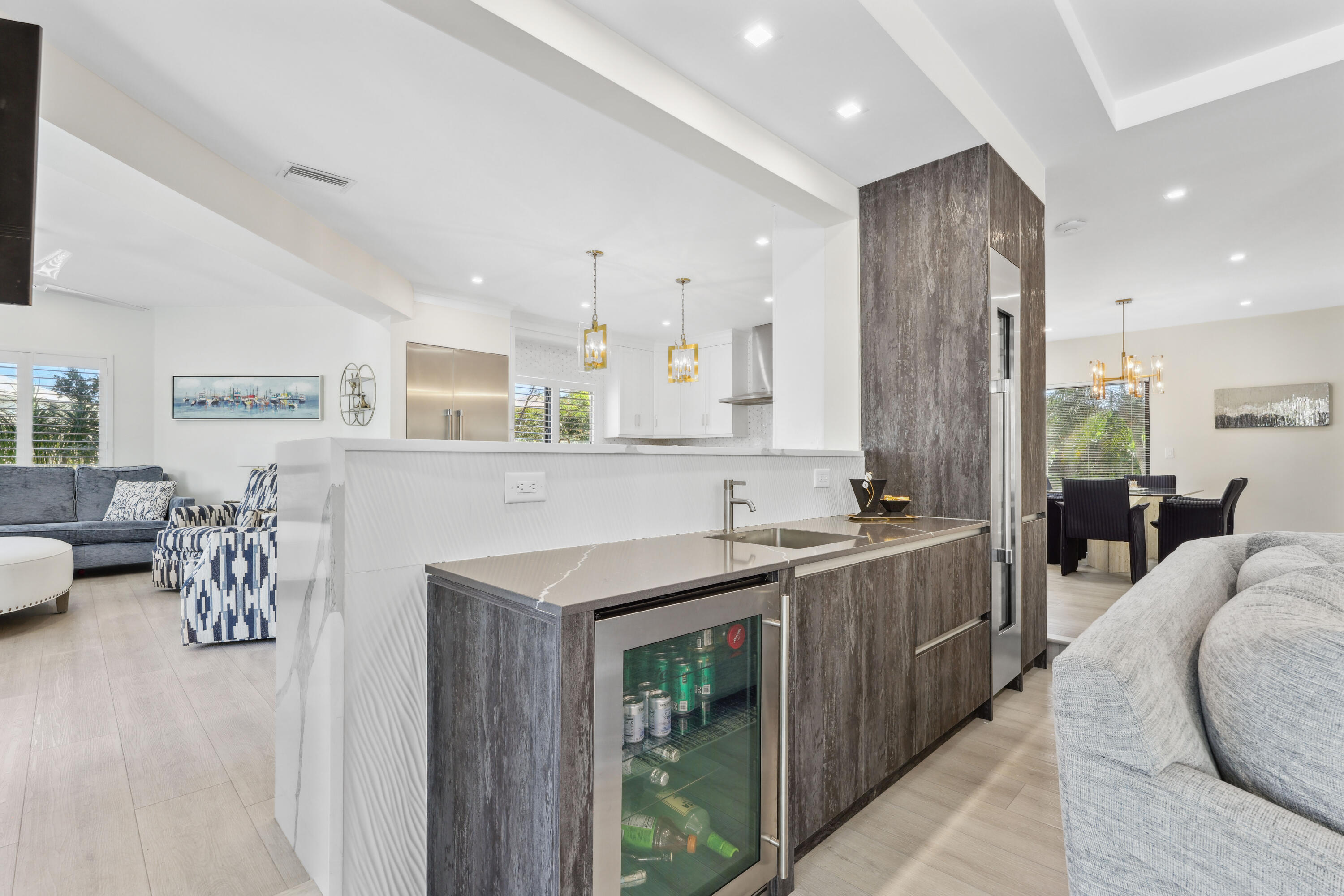 Open-plan kitchen with a dark-wood island, beverage refrigerator, and adjoining living and dining areas.