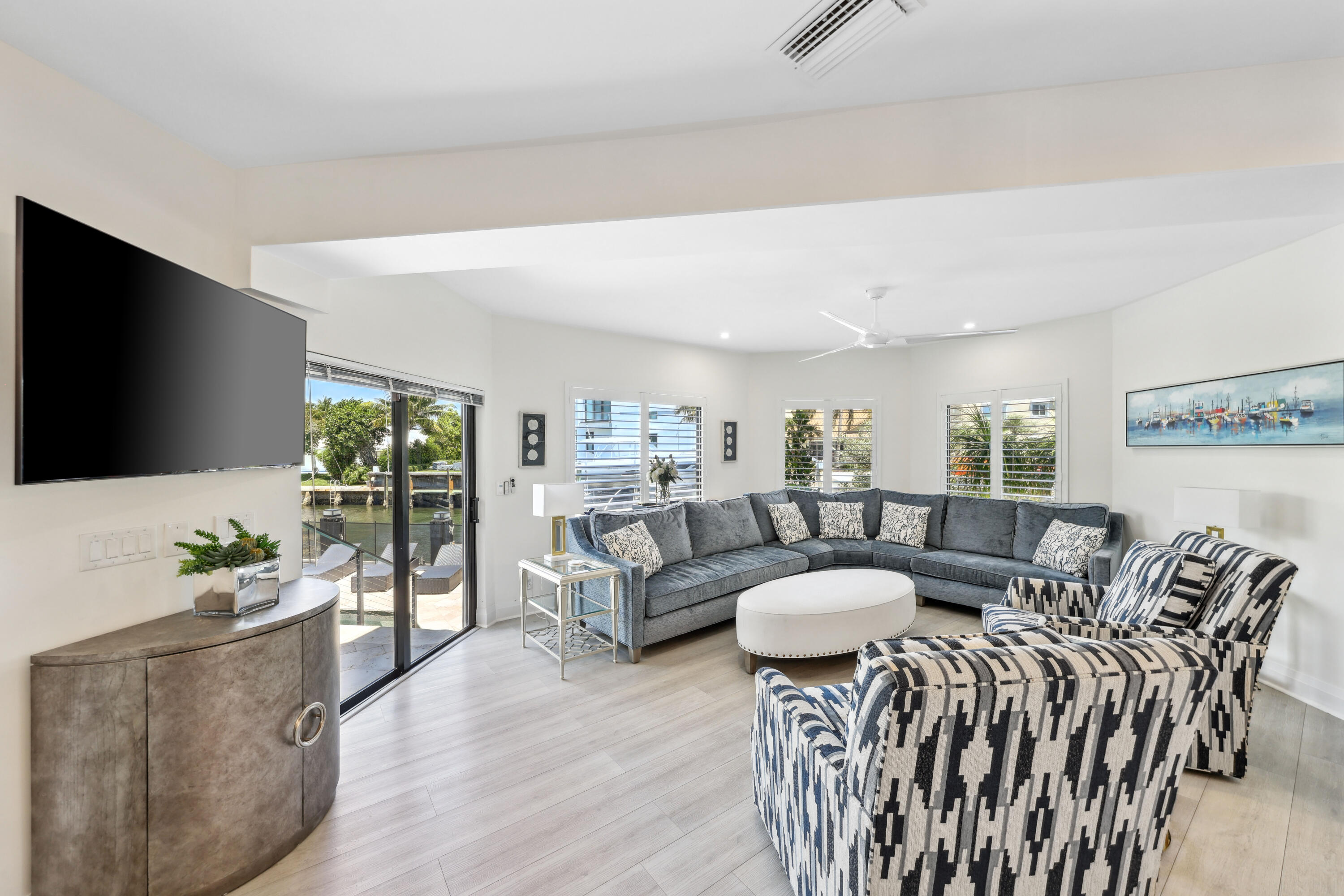 Bright living room with gray sectional and armchairs overlooking a canal through sliding glass doors.