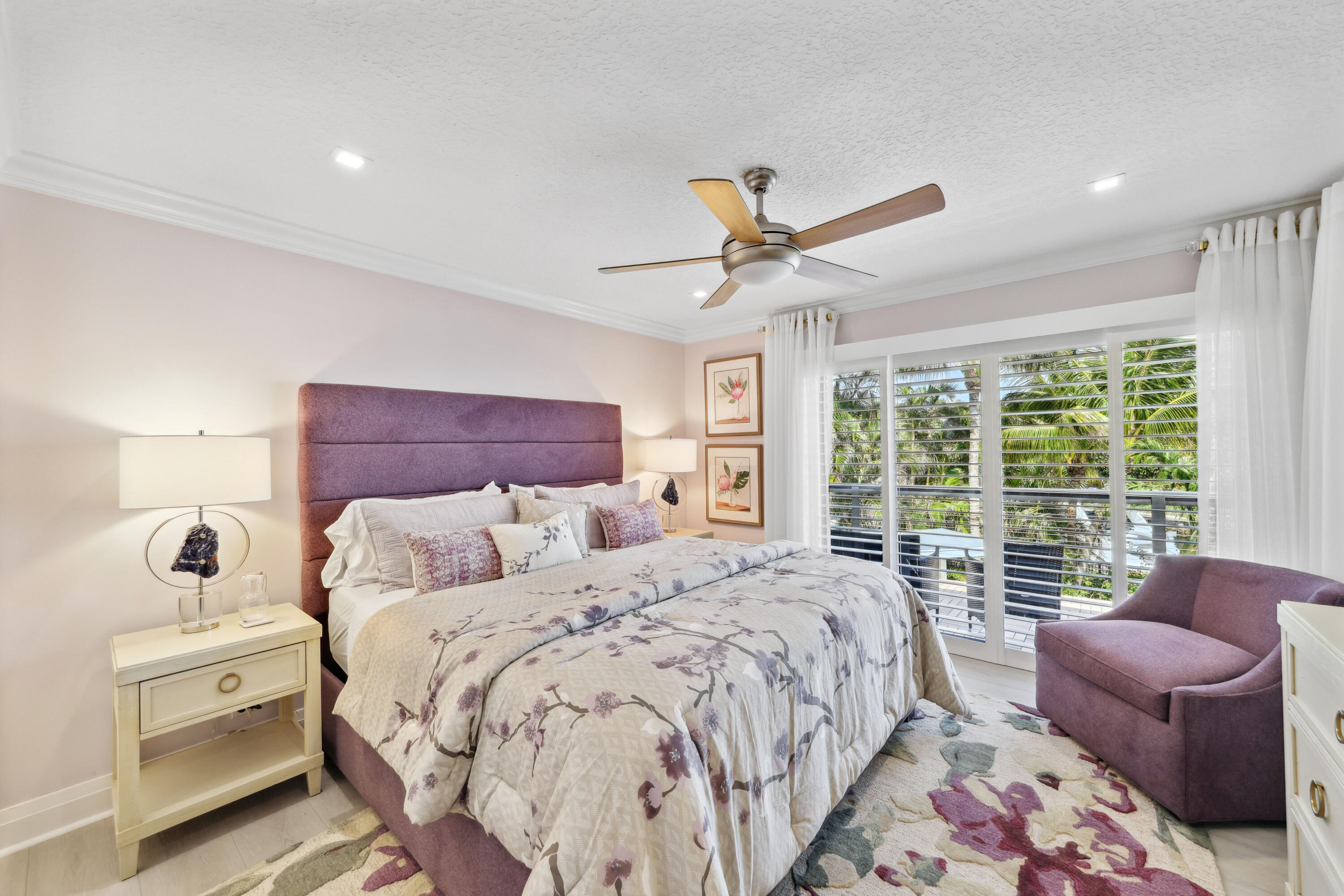 Bedroom with floral bedding, mauve furnishings, and plantation shutters overlooking palm trees.
