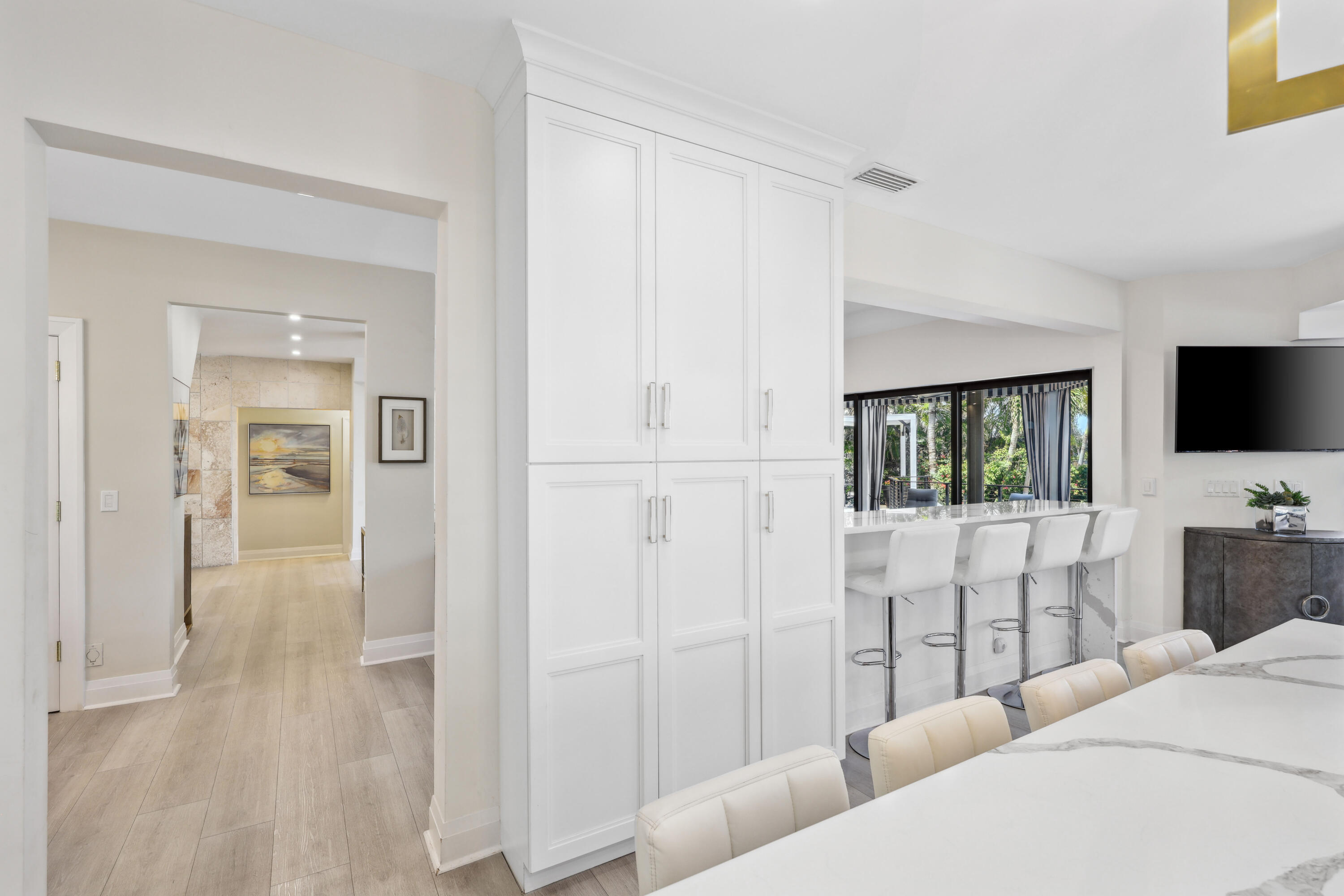 Bright kitchen with tall white cabinets, marble island, bar stools, and sliding doors to a leafy garden.