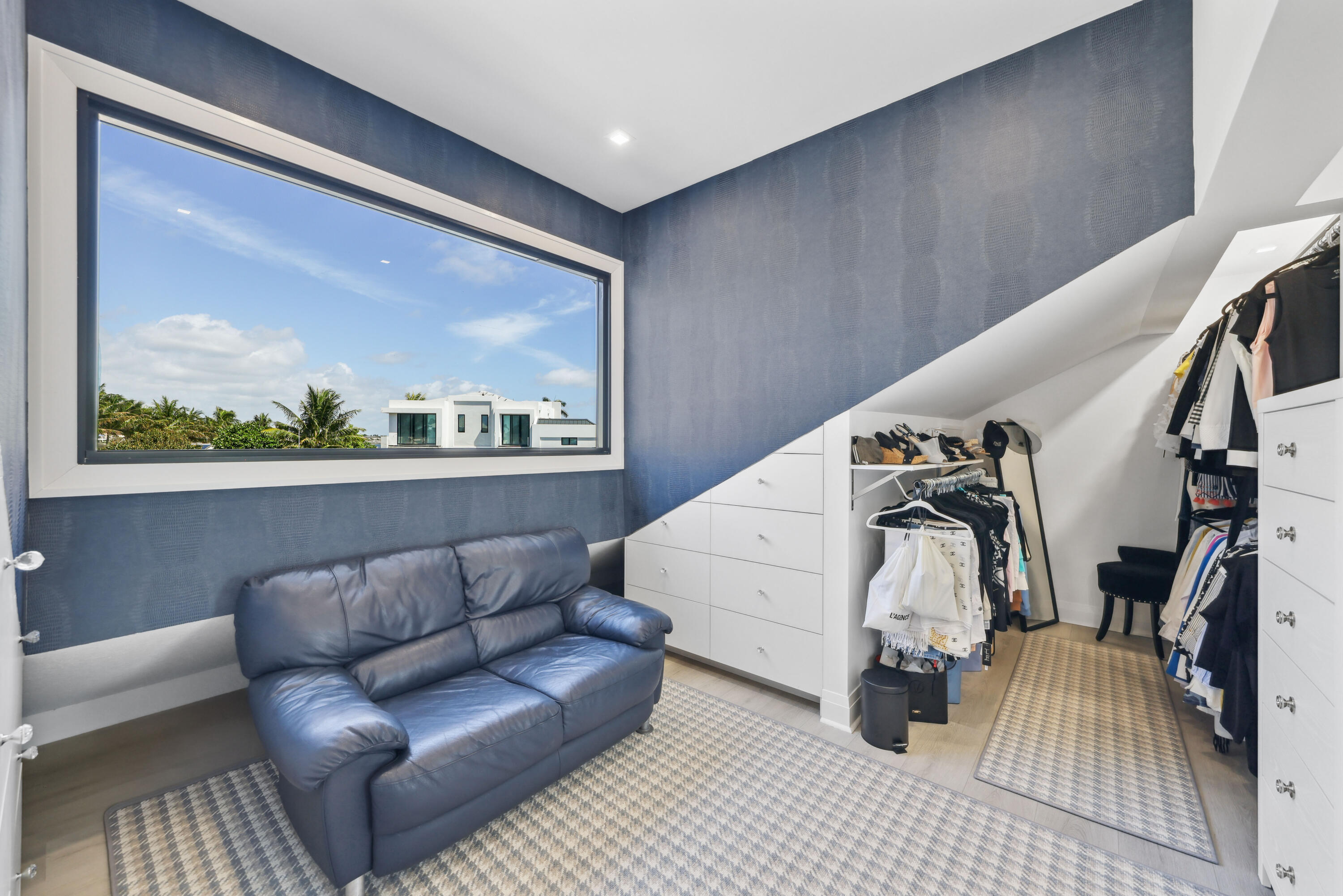 Walk-in closet with white built-ins, clothing racks, and a blue leather sofa beside a large window.