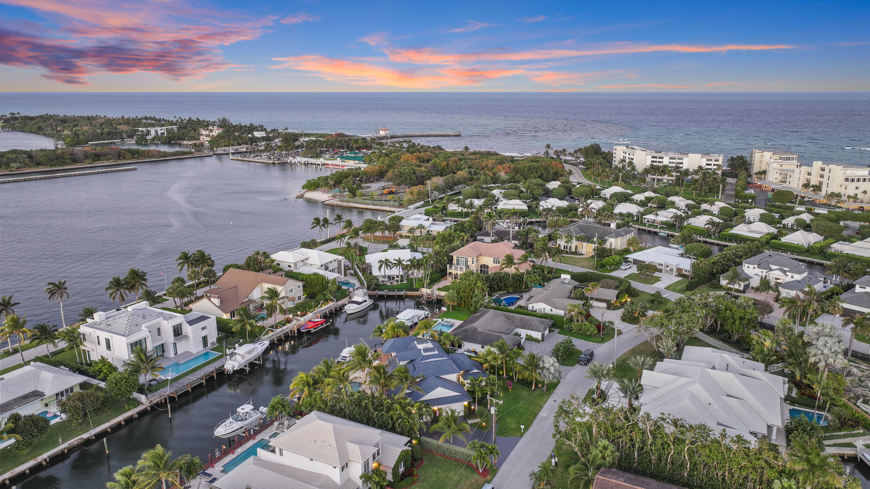 Aerial view of canal-front homes, docks, and the ocean beneath a pink dusk sky.
