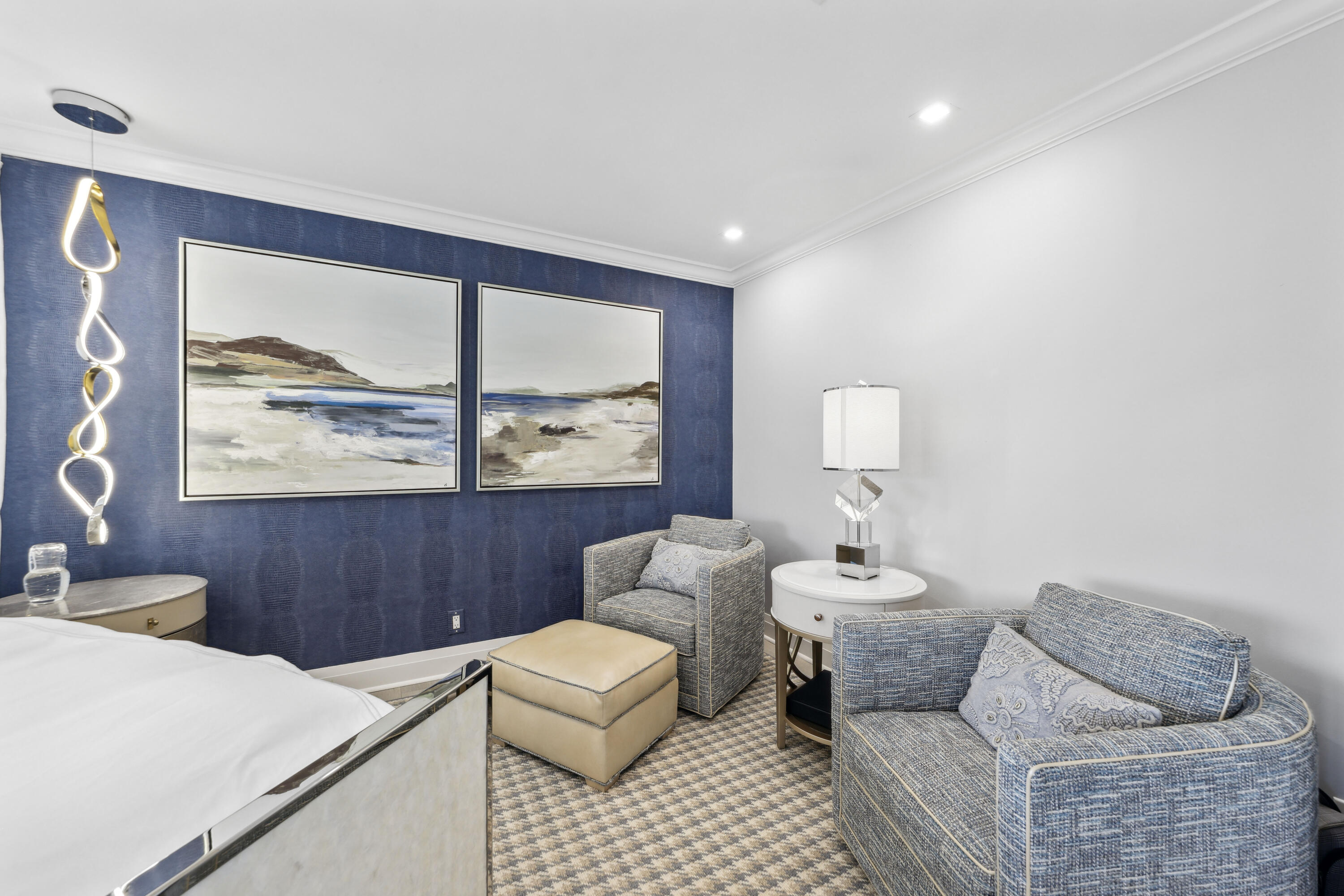 Furnished bedroom with a navy accent wall, two abstract paintings, and a cozy sitting area.