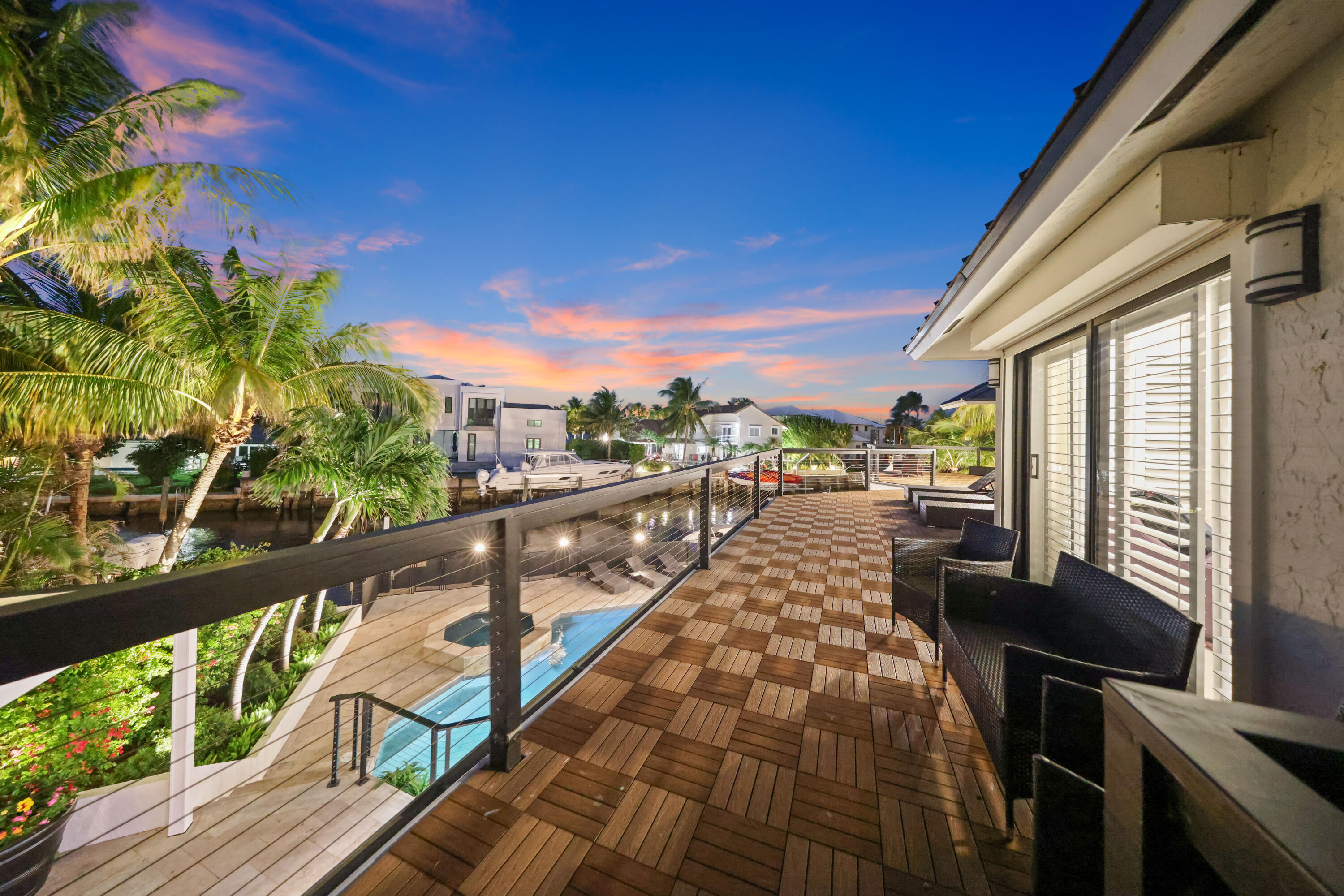 Waterfront balcony with wood decking and canal views beneath a pink sunset sky.
