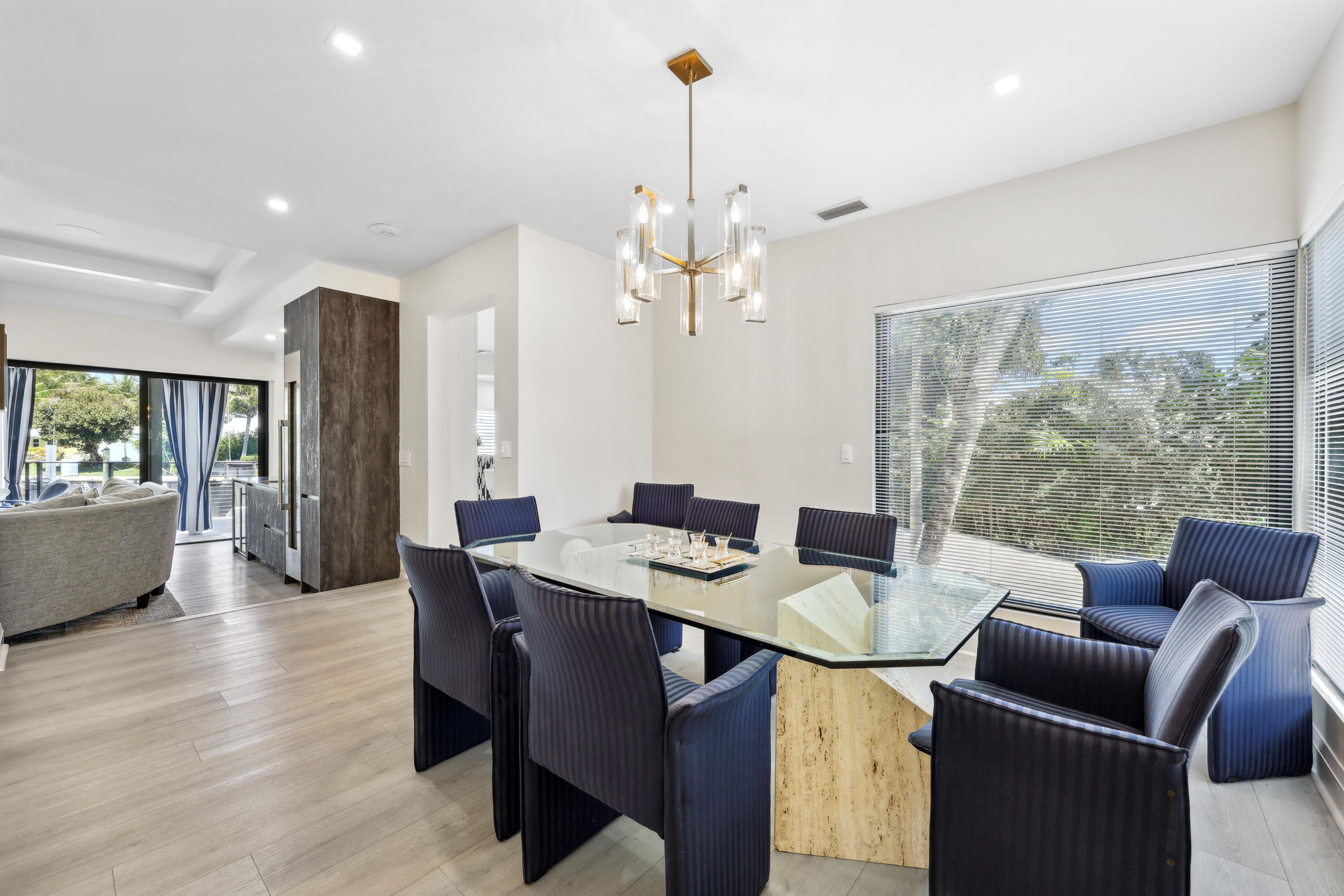 Dining room with a glass-top table, navy chairs, modern chandelier, and wide windows with blinds.