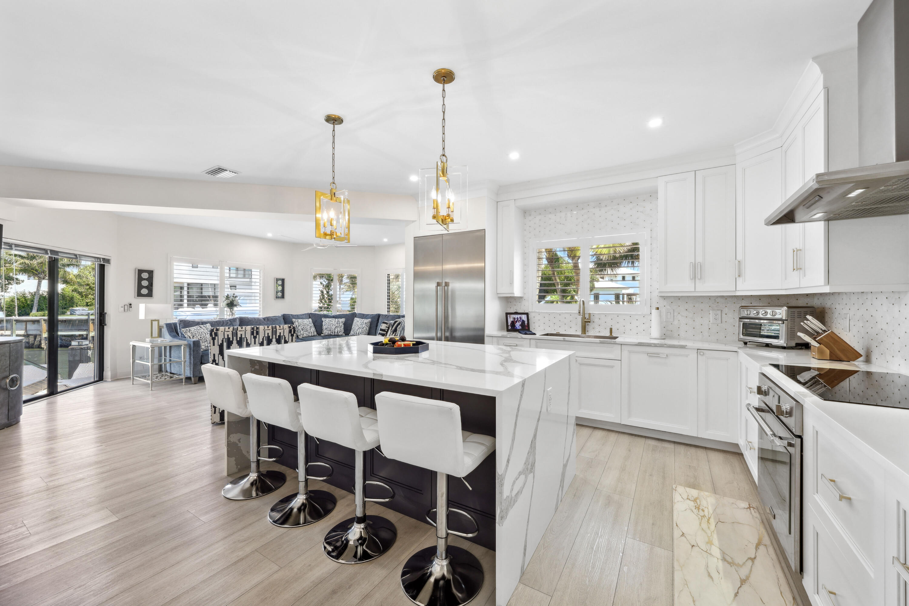 Bright white kitchen with a large marble-look island and bar seating beside an open living area.