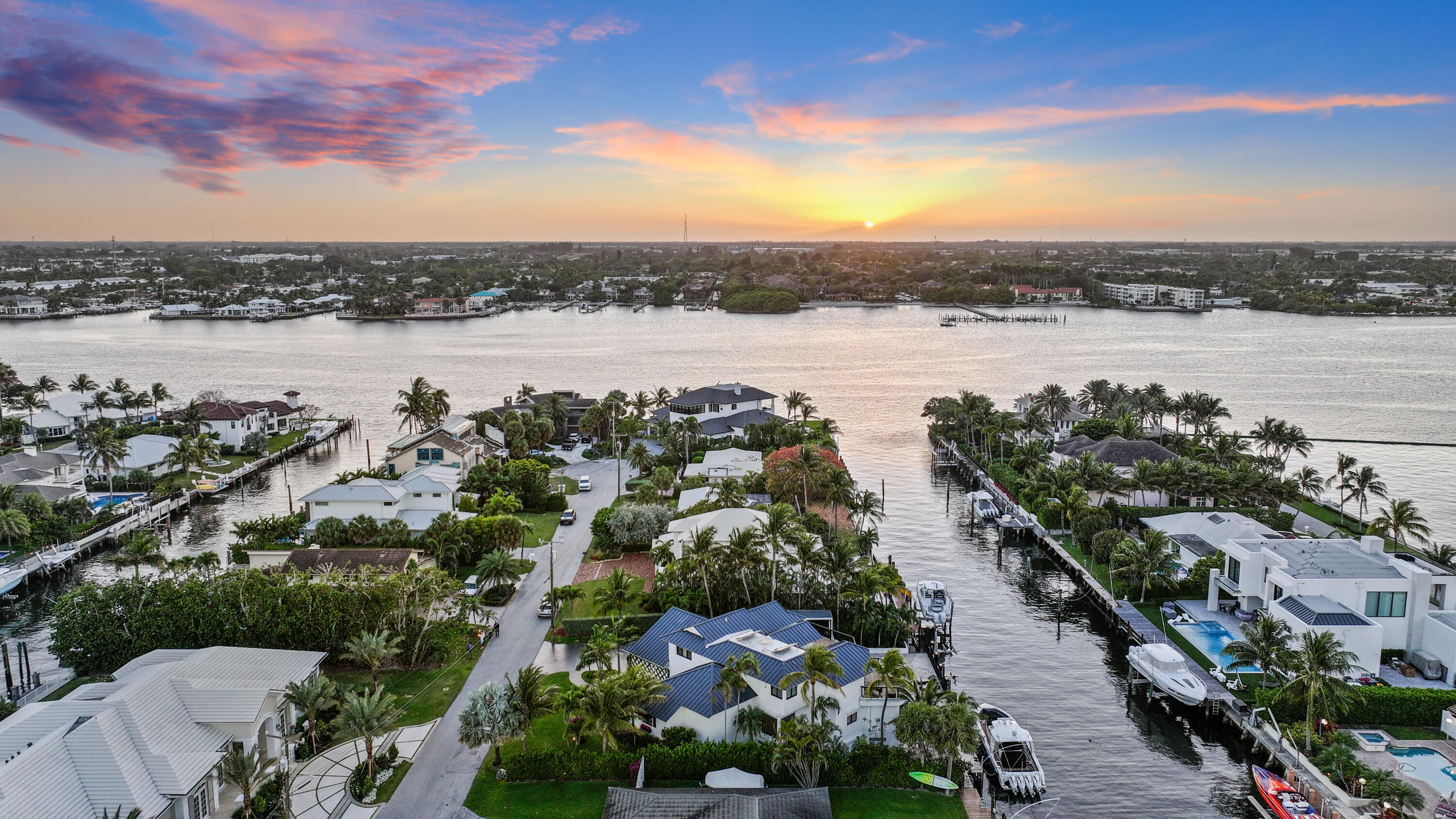 Aerial view of waterfront homes and docks along a broad waterway at sunset.