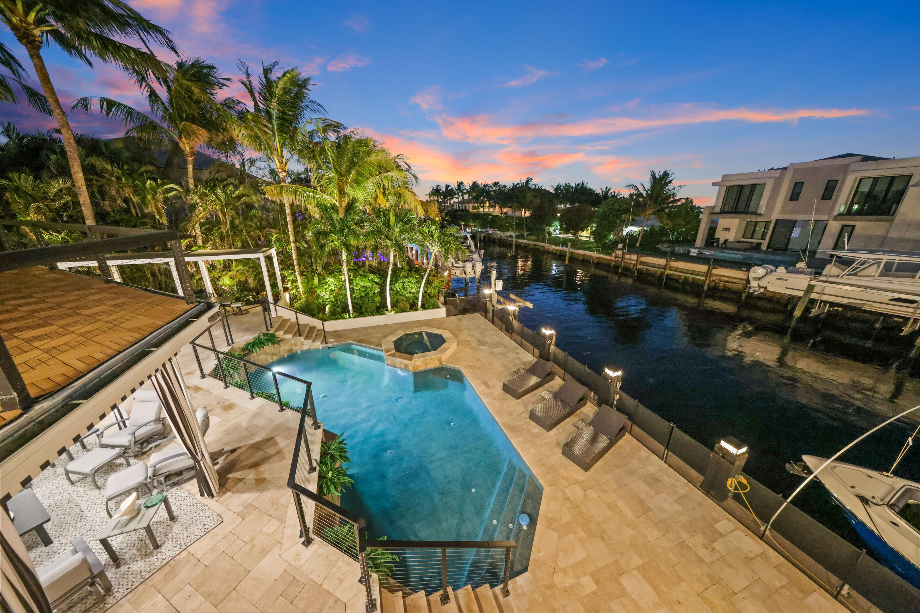 Waterfront pool and raised spa beside a palm-lined canal at dusk.
