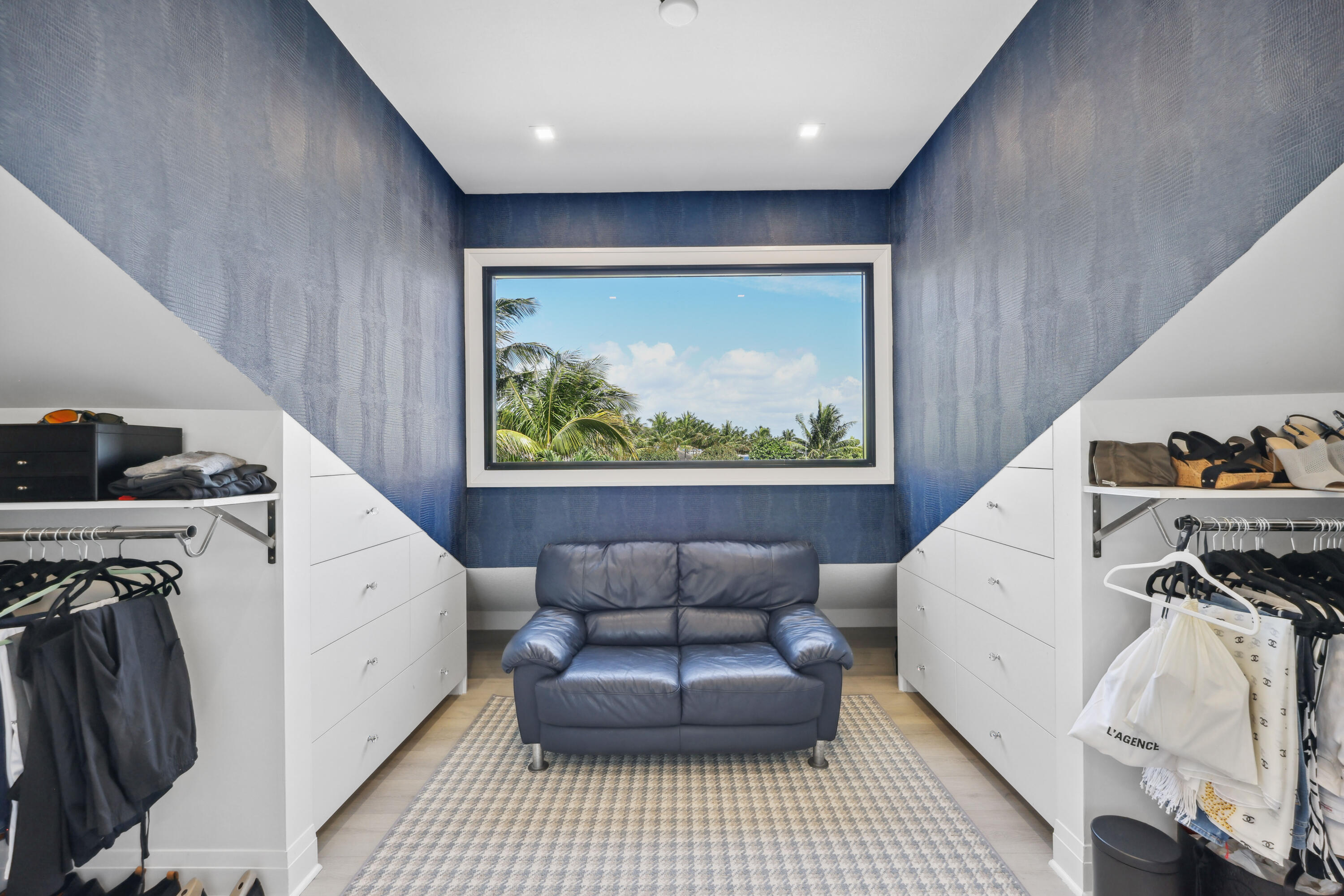 Walk-in closet with white built-ins, a blue loveseat, and a window overlooking palm trees.