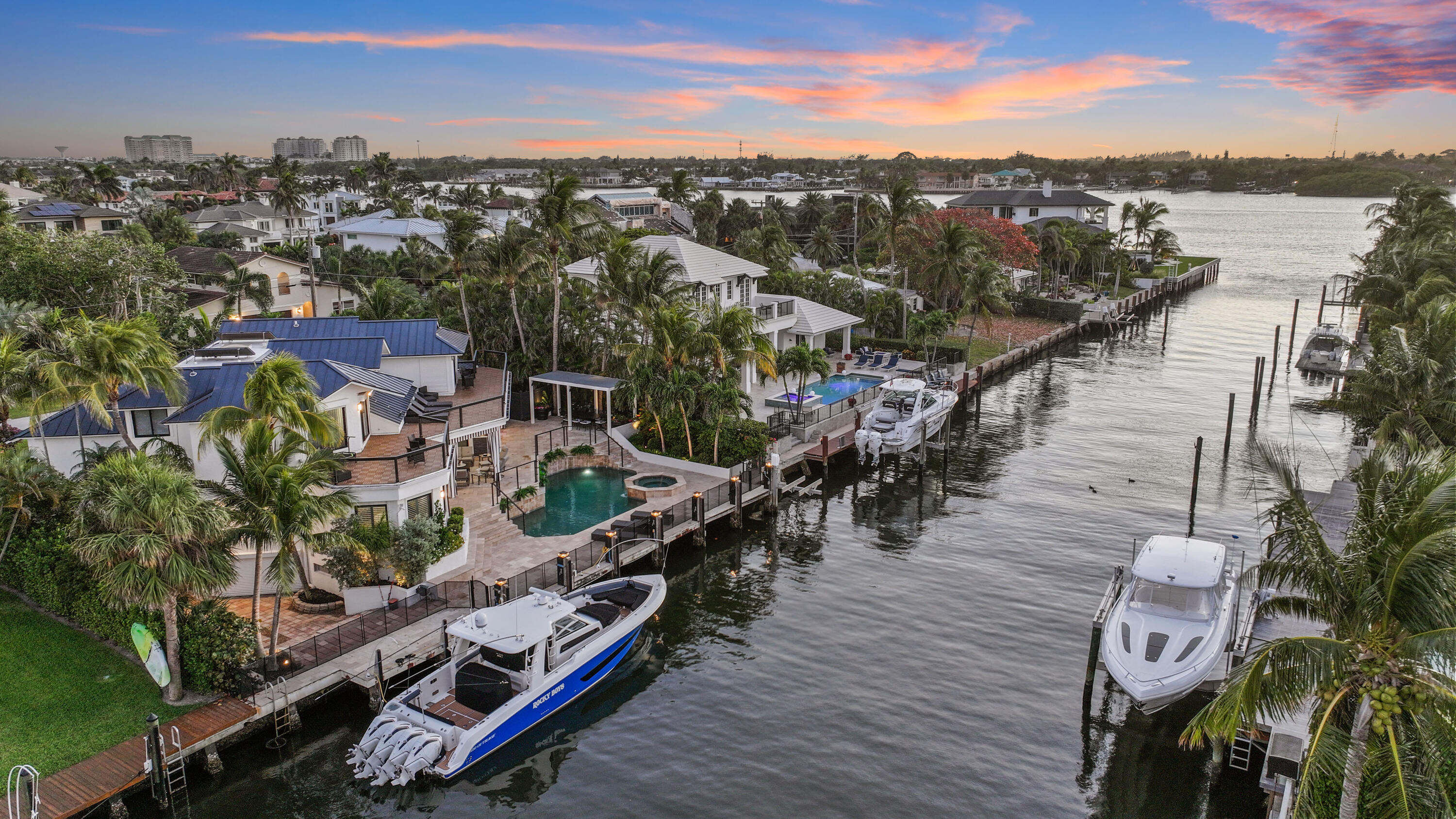 Waterfront home with a pool, private dock, and boats along a canal at sunset.