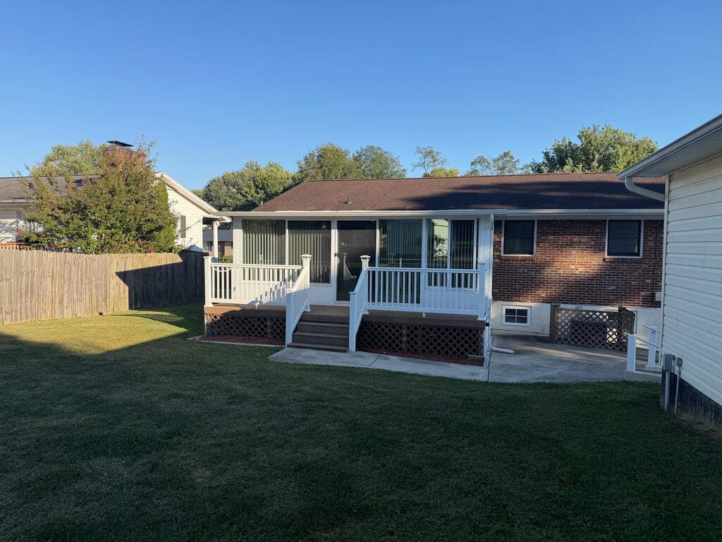 Brick home’s rear deck and enclosed sunroom overlook a broad lawn.