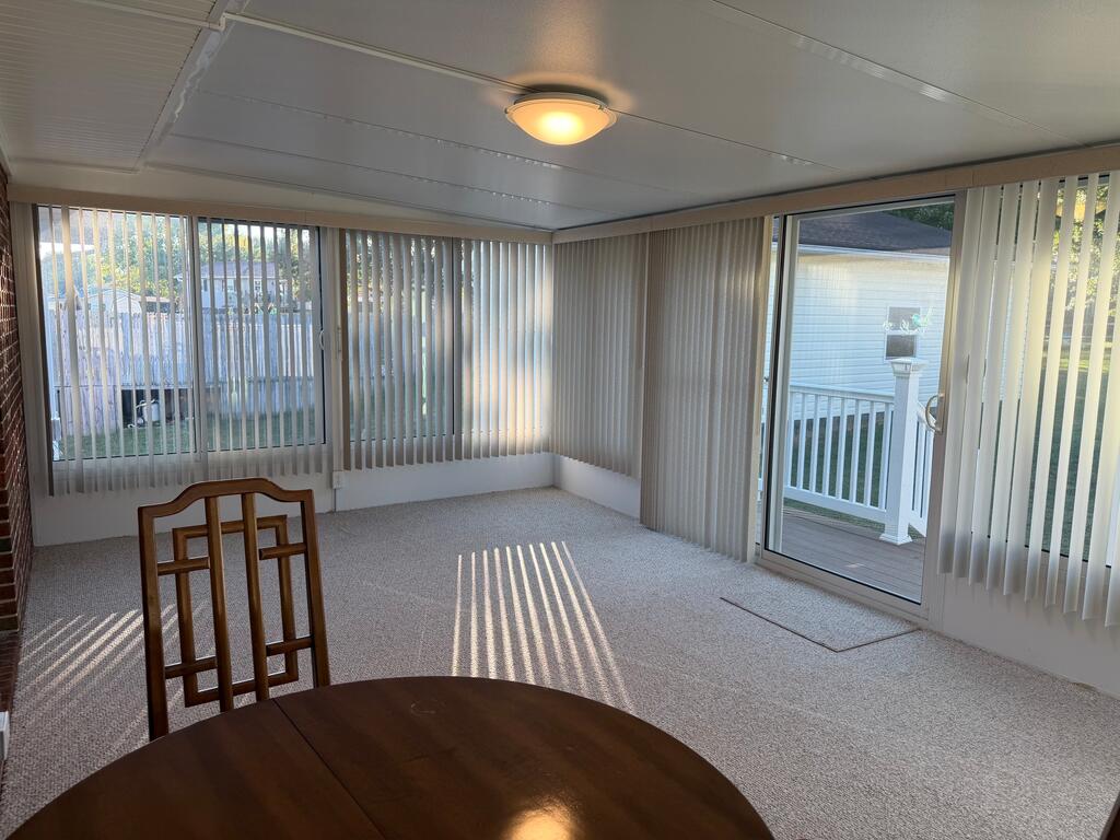 Carpeted sunroom with vertical blinds, a sliding glass door to the deck, and sunlight across the floor.
