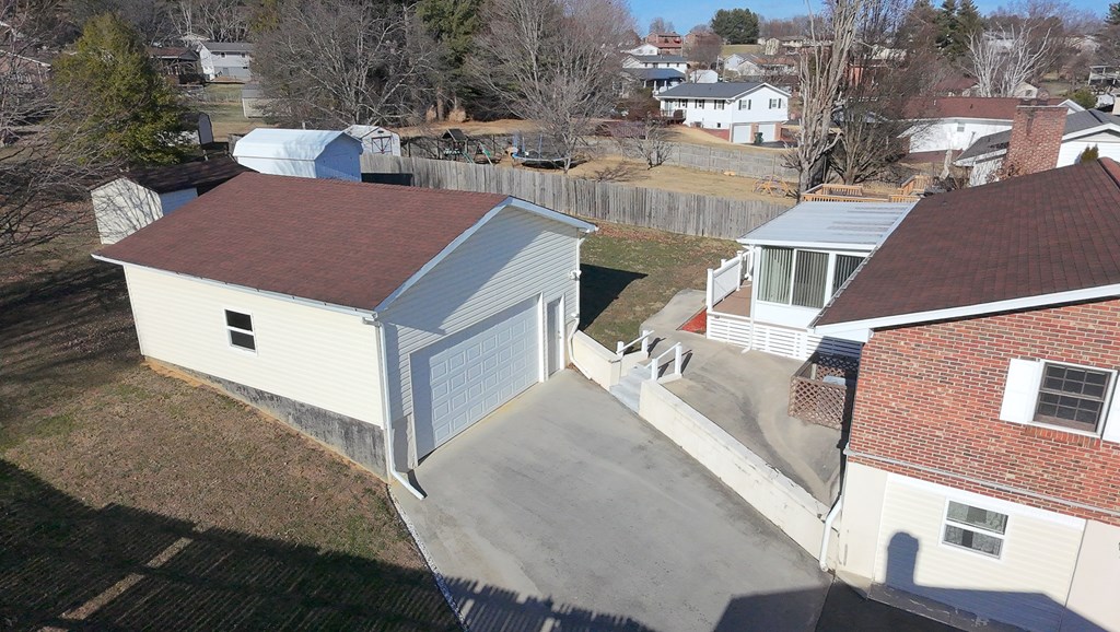 Aerial view of a brick house and detached garage with a wide concrete driveway and fenced yard.