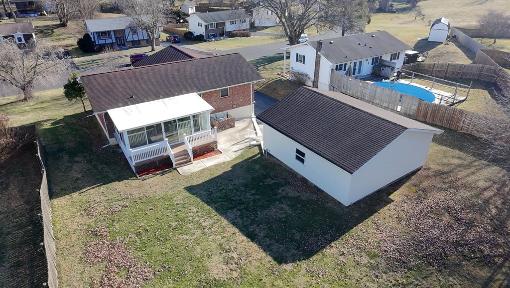 Aerial view of a brick home’s backyard, enclosed porch, and large detached garage.