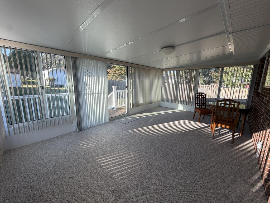 Enclosed sunroom with vertical blinds, carpet, and a sliding door opening onto a deck.