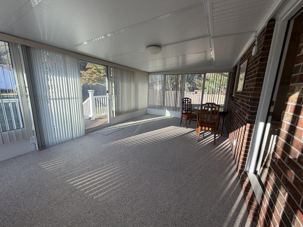 Enclosed sunroom with vertical blinds, sliding glass doors, carpet and a small wooden dining set.