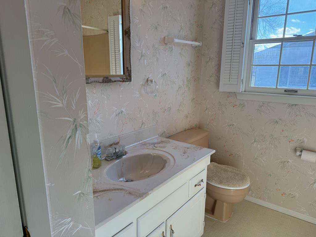 Bathroom with a white vanity, marble-pattern countertop, floral wallpaper, and a window with shutters.