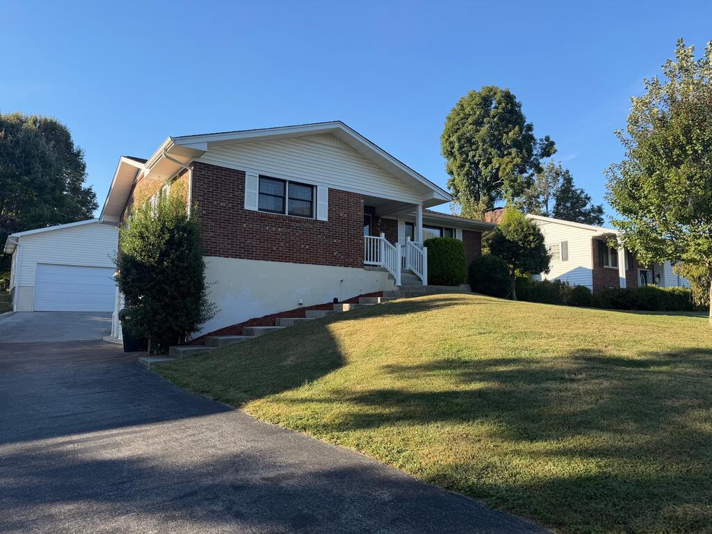 Brick home with attached garage, raised porch, and sloping front lawn.