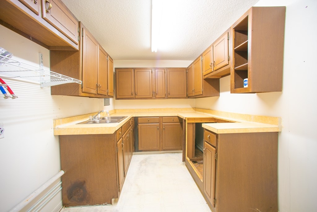 Utility room with brown cabinets, wraparound counters, a stainless-steel sink, and wire shelving.