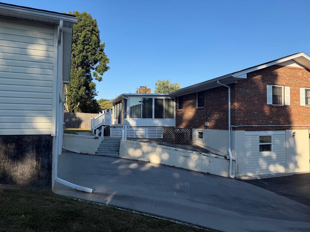 Brick house with a white enclosed porch, steps, and sloping paved driveway.