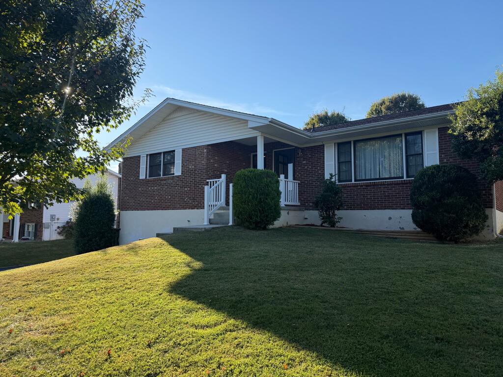 Single-story brick house with a covered entry and white railings above a sloping lawn.