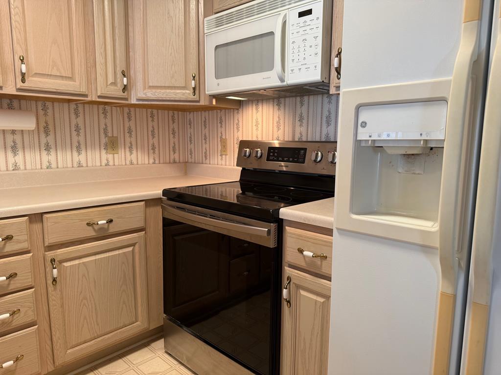 Kitchen with light wood cabinets, black electric range, over-the-range microwave, and refrigerator with water dispenser.