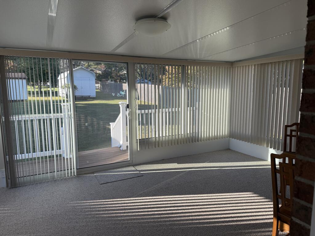 Carpeted sunroom with vertical blinds, sliding glass door, and sunlight casting striped shadows across the floor.