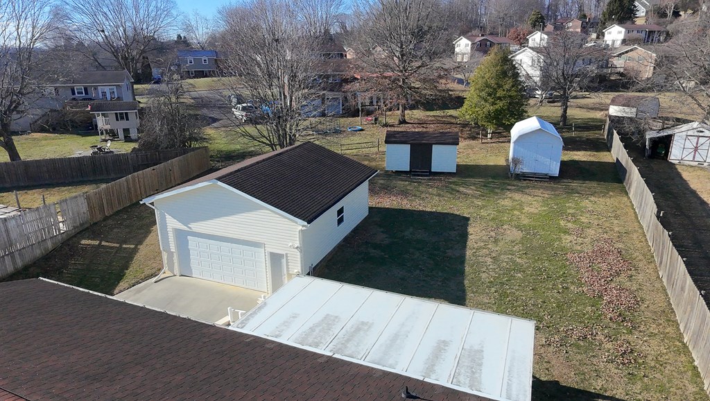 Aerial view of a fenced backyard with a detached garage and two sheds.