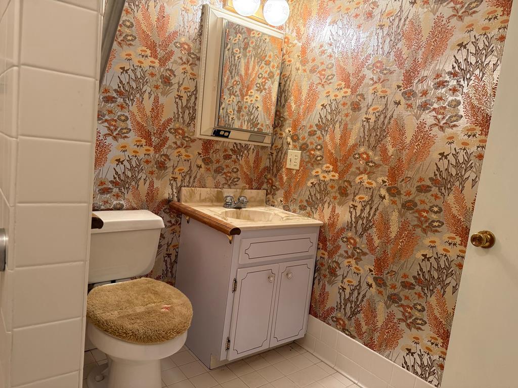 Bathroom with bold floral wallpaper, a white vanity, and a toilet with a tan cover.