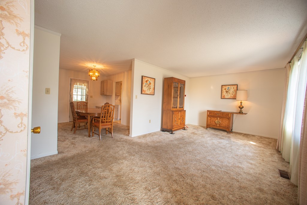 Living room with beige carpet, wooden display cabinets, and an adjoining dining area.