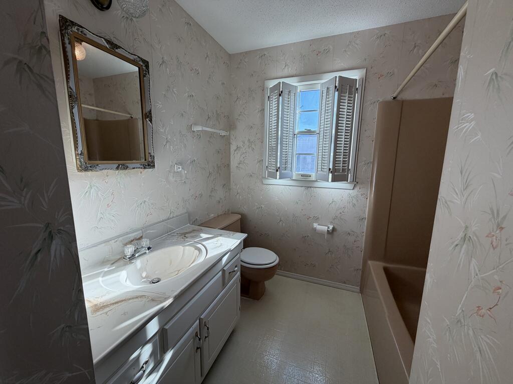 Bathroom with a long white vanity, shuttered window, and curtained bathtub-shower.
