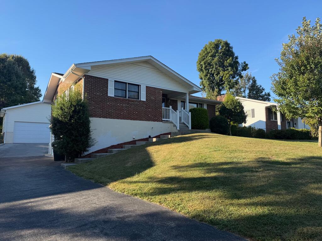 Brick ranch home with an attached garage, raised front steps, and a sloping lawn.