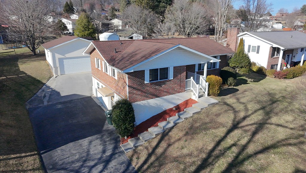 Aerial view of a brick split-level home with a wide driveway, attached garage, and front steps.