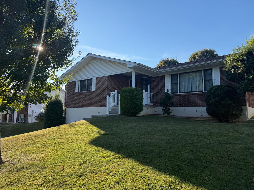 Single-story brick house with a white-railed porch and sloping front lawn.