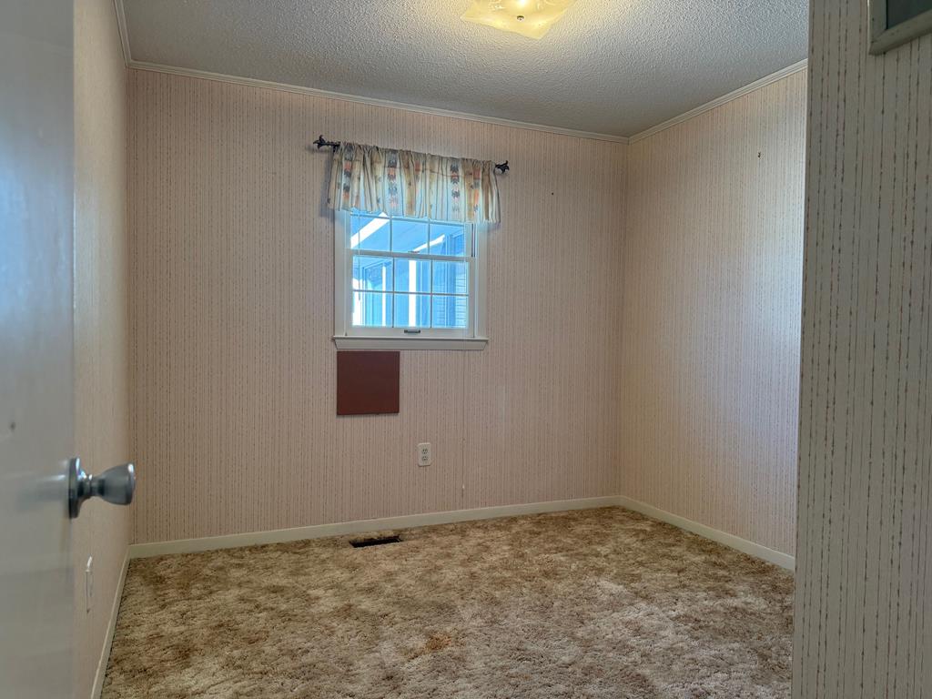 Empty bedroom with beige striped wallpaper, brown carpet, and a curtained window.