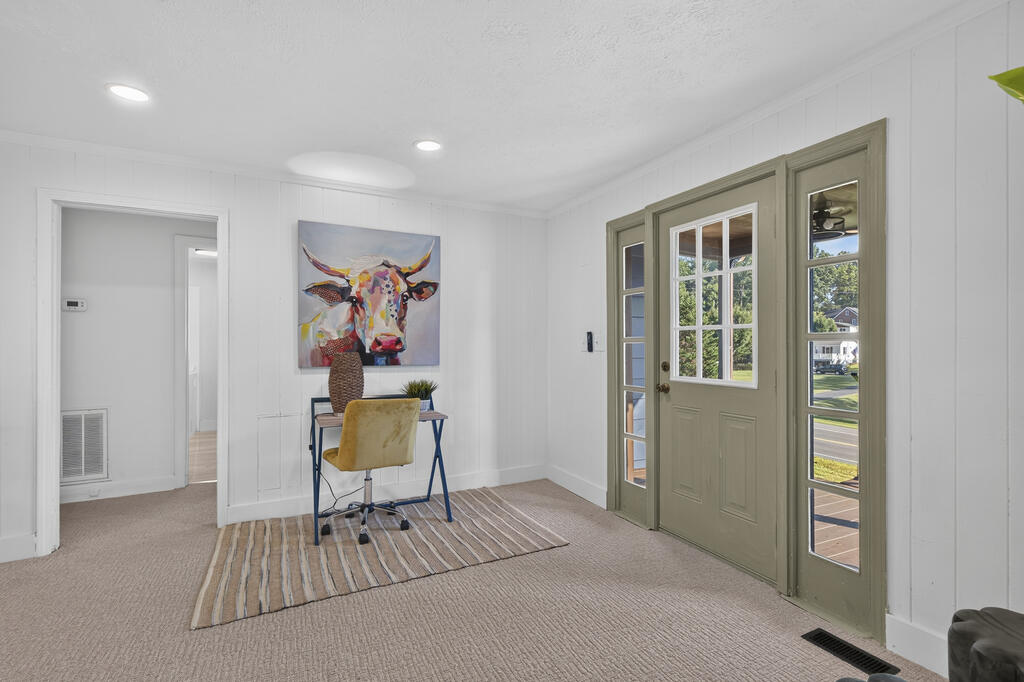 Entryway with sage-green glass-paneled front door, small desk, yellow chair, and colorful longhorn artwork.