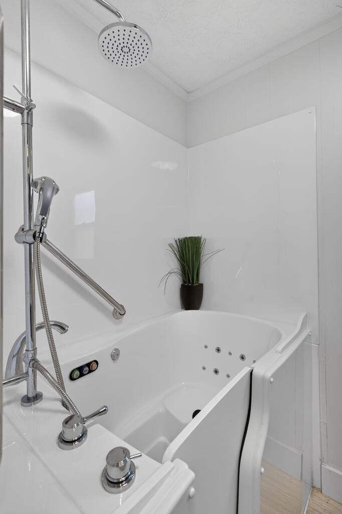 White walk-in jetted bathtub with a built-in seat, chrome shower fixtures, and a small potted plant.