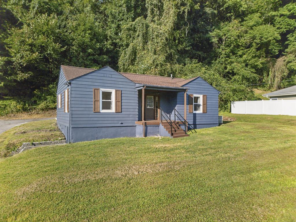 Blue single-story house with brown shutters, covered porch, and sloping front lawn.