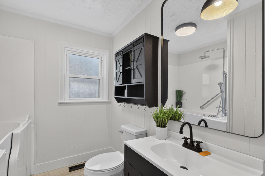Bathroom with a dark vanity, large mirror, white bathtub, and frosted window.