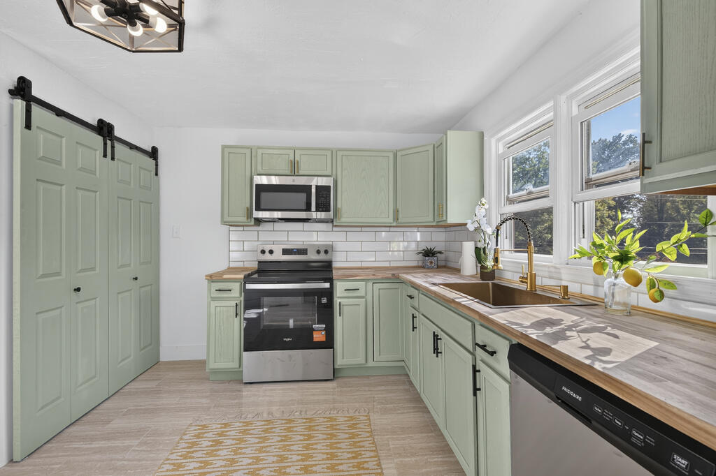 Kitchen with sage-green cabinets, butcher-block counters, and a farmhouse sink beneath bright windows.